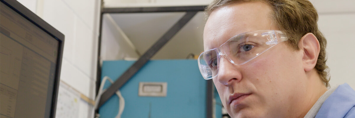 A scientist looks past his computer at his testing equipment