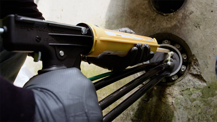 FST cartridge pumped with a dispensing gun into a duct in a concrete wall. Some black wires protrude from the duct.