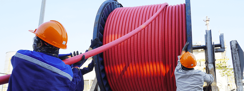 Two workers pulling conduit from a large reel