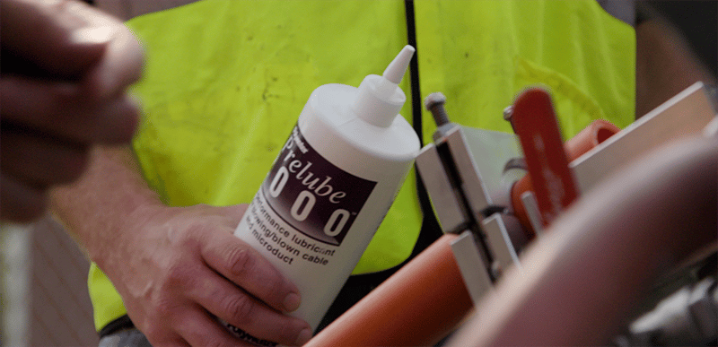 A bottle of Polywater Prelube lubricant is used with a cable blowing machine