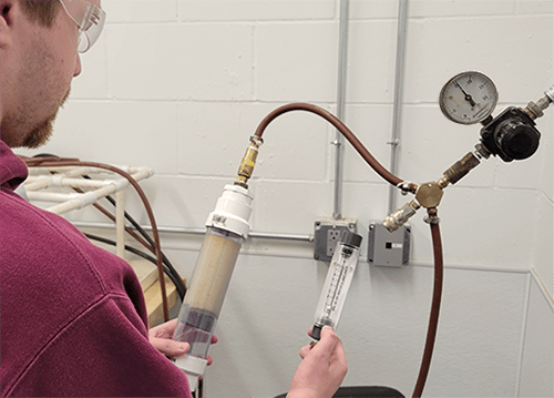 A chemist holds up a pneumatic pressure testing mechanism and checks the results