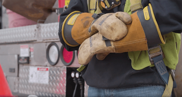 Un monteur de lignes électriques portant des gants de protection individuelle en caoutchouc devant son camion-nacelle.