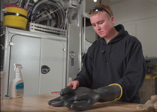 Un monteur de lignes électriques examine ses gants de protection en caoutchouc sur une table avant de les nettoyer.
