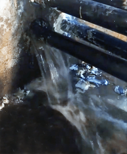 De l’eau jaillit d’un trou dans un mur en béton d’où sortent des tuyaux noirs.