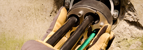 Una mano con guante empuja un sello mecánico de metal en la apertura de un ducto con cuatro cables que salen de él.