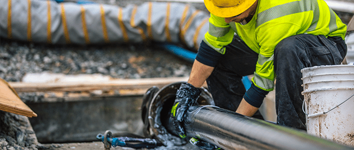 Ein Arbeiter in einem neongrünen Sicherheitshemd reibt ein sehr großes Hochspannungskabel mit Schmiermittel ein, während es in ein Rohr gezogen wird.