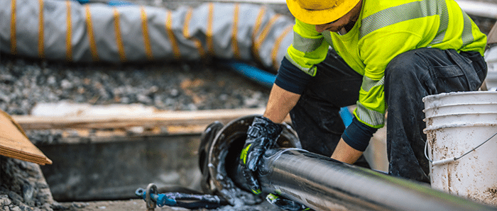 A worker in a neon green safety shirt rubs lubricant on a very large high-voltage cable as it is pulled into a duct.