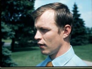 The side profile of a young man with brown hair wearing a blue collared shirt.