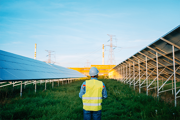 Man walking in green grass between solar arrays with HV power lines in the distance