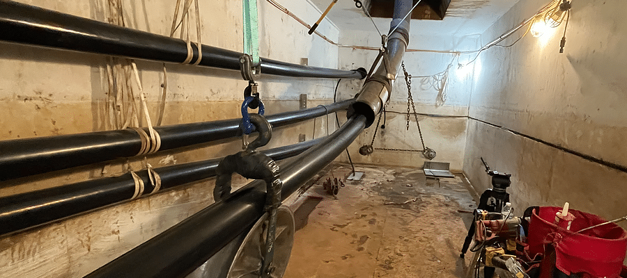 Vue de plusieurs câbles haute tension traversant une voûte souterraine en béton gris. Un seau rouge avec des outils de travail est visible dans le coin.