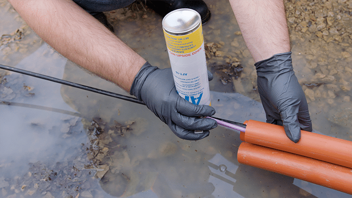 An upside-down can of Polywater AFT being deployed into an orange communications duct with a black cable coming out of it.