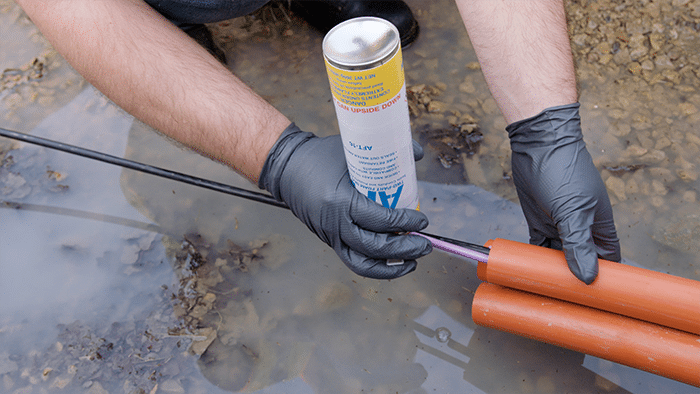 Eine umgedrehte Dose Polywater AFT wird in einen orangefarbenen Kommunikationsrohr eingesetzt, aus dem ein schwarzes Kabel herauskommt.