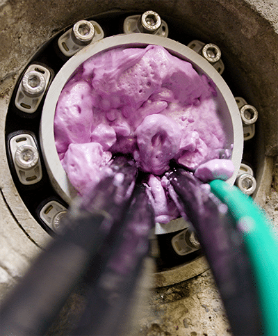 A conduit set in concrete is filled with a purple-foam sealant called Polywater AFT. Some black cables and a green cable come out of the conduit towards the viewer.