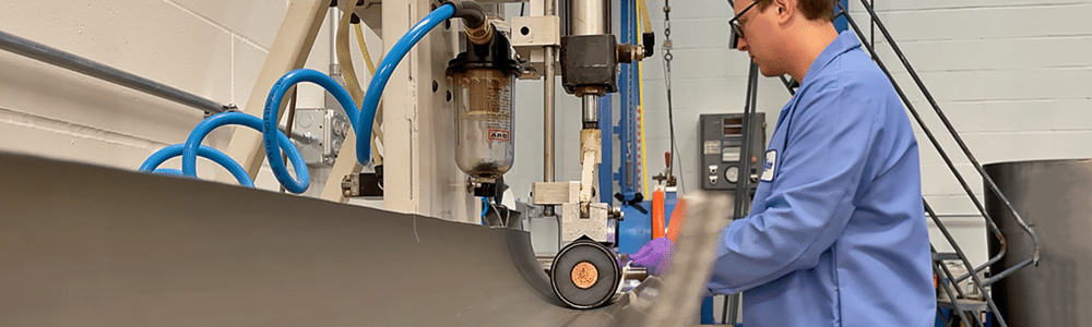 A chemist in a blue lab coat watches a section of black HD cable on the Polywater Friction Table as it slides through.