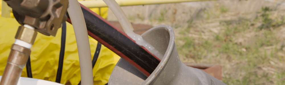 A black and red electrical cable enters a conduit while a white lubricant is pumped through a hose and is applied to the cable.