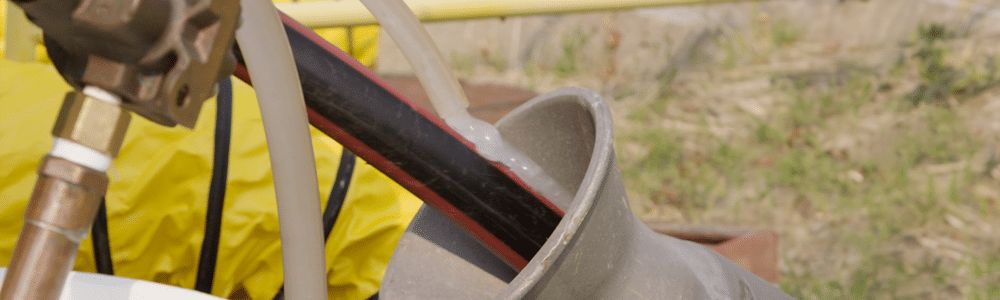 Un câble électrique noir et rouge entre dans un conduit tandis qu'un lubrifiant blanc est pompé dans un tuyau et appliqué sur le câble.