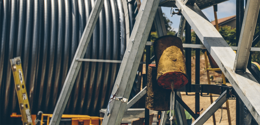 Un esparcidor de lubricante compuesto por dos esponjas grandes cuelga de un andamiaje frente a un gran carrete de cable eléctrico de alto voltaje.