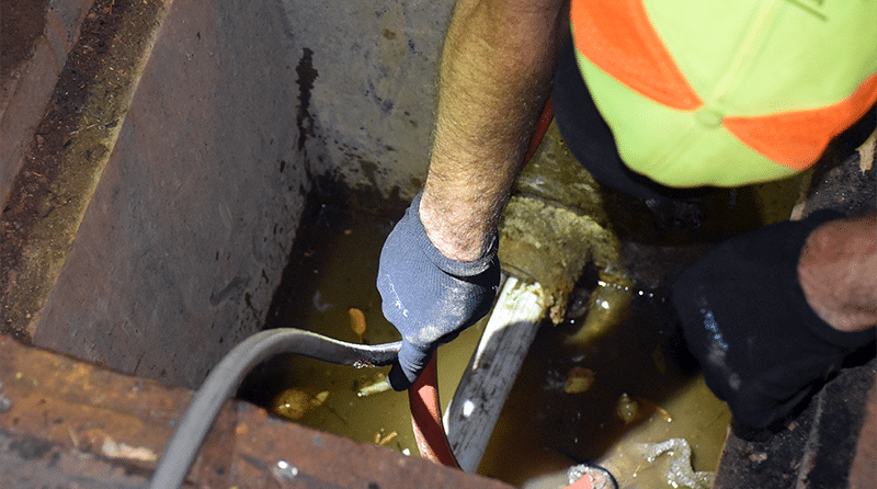 Un hombre en una bóveda de fibra óptica húmeda sostiene una manguera mientras bombea Polywater IceFree hacia un conducto de fibra óptica para evitar que se llene de agua y se congele.