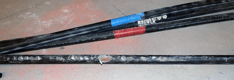 Tres cables eléctricos negros en el suelo que muestran signos de desgaste. La funda del cable inferior se ha quemado y deja al descubierto el cable eléctrico que hay en su interior.