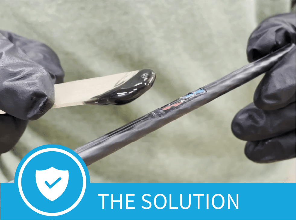 A black paste-Polywater CJR Cable Jacket Repair- on the end of a popsicle stick, is spread on the damaged area of a fiber cable jacket.