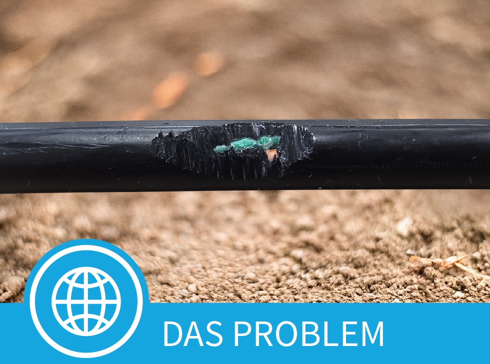 Ein beschädigter Kabelmantel eines Glasfaserkabels, der freiliegende Glasfaserkabel über einem schmutzigen Hintergrund zeigt. Am unteren Rand des Bildes stehen die Worte 