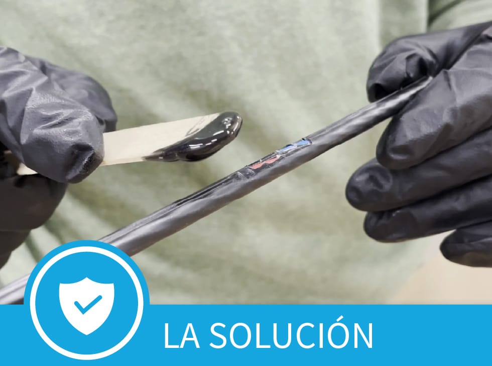 Una pasta negra - Polywater CJR Reparación de Chaqueta de Cable - en el extremo de un palillo de helado, se extiende sobre el área dañada de la chaqueta del cable de fibra. En la parte inferior de la imagen se muestran las palabras,