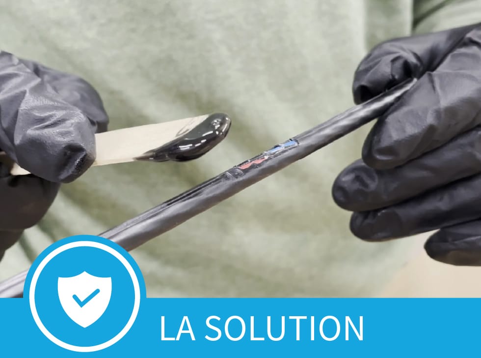 Une pâte noire - Réparation de gaine de câble Polywater CJR - sur l'extrémité d'un bâtonnet de glace, est étalée sur la zone endommagée d'une gaine de câble à fibre optique. En bas de l'image, on peut lire les mots 