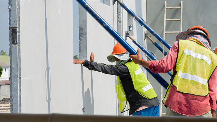 Due operai nei giubbotti di sicurezza aiutano a sostenere alcune pareti prefabbricate in cemento.