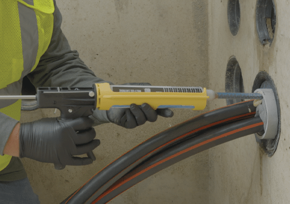 A worker in a concrete vault holds a Polywater FST cartridge in a yellow dispensing tool.